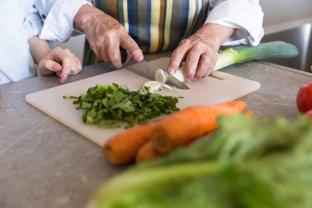 Cerca de una dama senior cortar verduras en un tablero