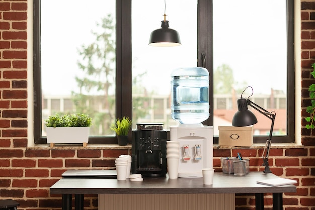 Cerca del dispensador de agua y máquina de café en la mesa en la oficina de reuniones. Refresco líquido para personas que trabajan en lugares de trabajo modernos. Equipo de bebidas frescas para hidratarse en el descanso.