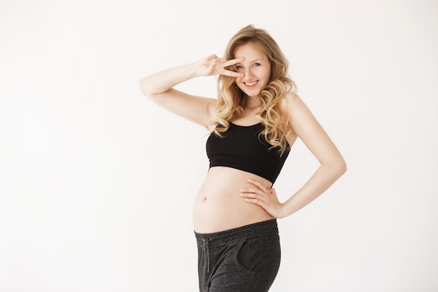 Cerca de la divertida y joven mamá europien guapa con cabello rubio en ropa acogedora sonriendo alegremente