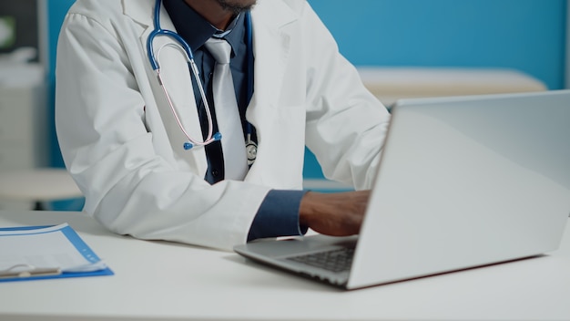 Cerca del doctor escribiendo en el teclado de la computadora portátil en el gabinete médico