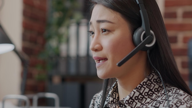 Cerca del empleado del centro de llamadas con auriculares hablando por teléfono sobre telemarketing con clientes. Mujer con micrófono para telecomunicaciones con personas de atención al cliente.