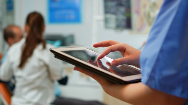 Cerca de la enfermera sosteniendo y escribiendo en tableta de pie en la clínica estomatológica, mientras que el médico está trabajando con el paciente en segundo plano. Uso del monitor con pantalla de pc de maqueta de clave de pc izolated chroma key