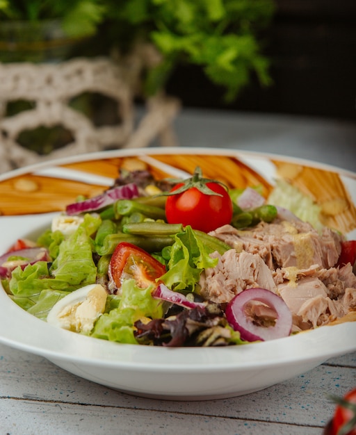 Cerca de ensalada de atún con huevos, cebolla, lechuga, tomate y guisantes.