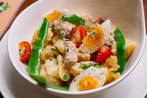 Cerca de ensaladera de patata italiana con atún frijoles tomate cherry perejil huevos duros y aceite de oliva