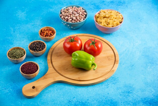 Cerca de la foto. Tomate y pimiento sobre tabla de madera delante de dos tazón. Frijoles y pasta.