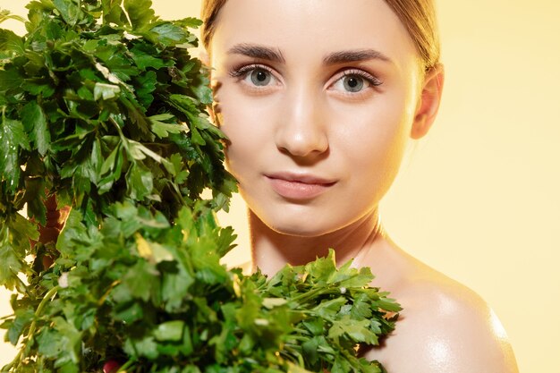 Cerca de hermosa mujer joven con hojas verdes sobre blanco