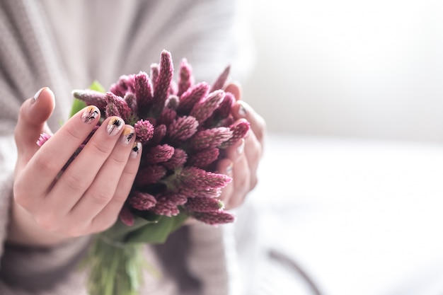 Cerca de hermosas manos femeninas con gran taza blanca de café capuchino y flores.