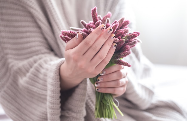 Cerca de hermosas manos femeninas con gran taza blanca de café capuchino y flores.