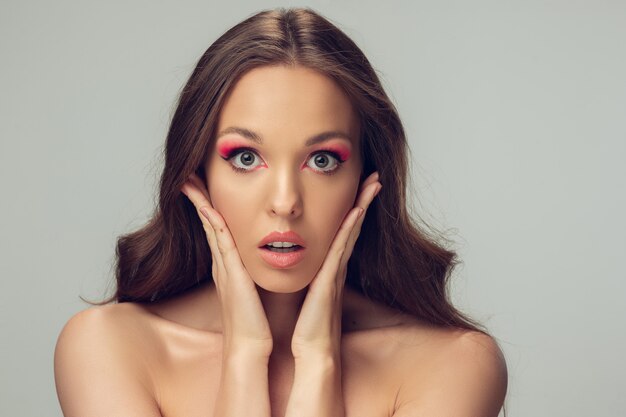 Cerca del hermoso rostro femenino, labios con maquillaje elegante brillante aislado en gris