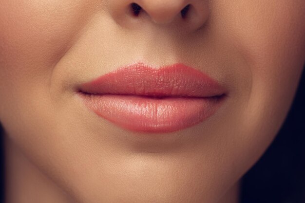 Cerca del hermoso rostro femenino, labios con maquillaje elegante brillante aislado en gris