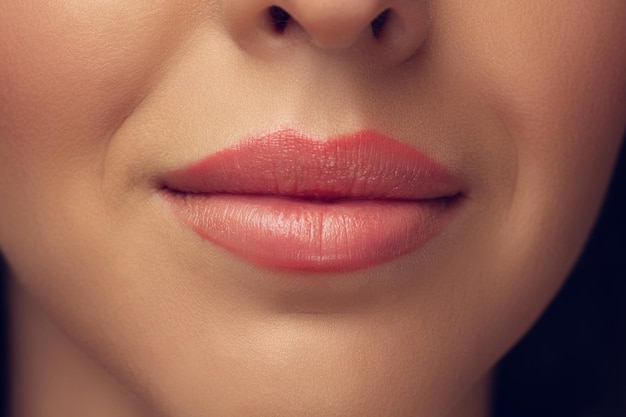 Cerca del hermoso rostro femenino, labios con maquillaje elegante brillante aislado en gris