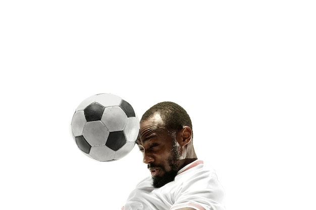 Cerca del hombre africano emocional jugando al fútbol golpeando la pelota con la cabeza en la pared blanca aislada. Fútbol, deporte, expresión facial, emociones humanas, concepto de estilo de vida saludable. Copyspace.