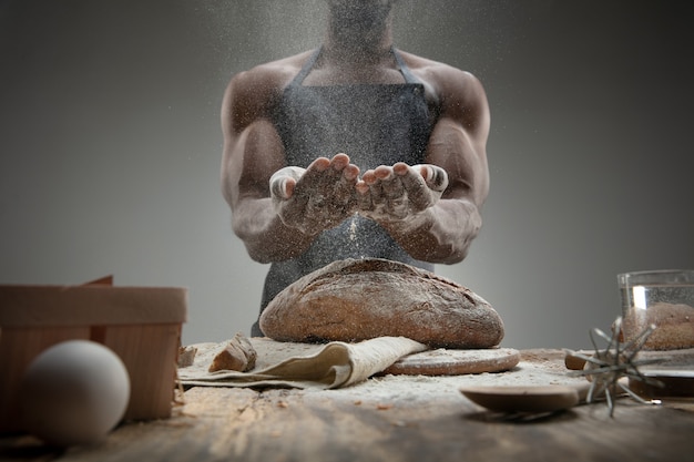 Cerca del hombre afroamericano cocina cereales frescos, pan, salvado en la mesa de madera. Comida sabrosa, nutrición, producto artesanal. Alimentos sin gluten, estilo de vida saludable, fabricación ecológica y segura. Hecho a mano.