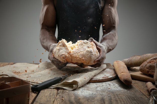 Cerca de hombre afroamericano cocina cereales frescos, pan, salvado en la mesa de madera. Comida sabrosa, nutrición, producto artesanal.