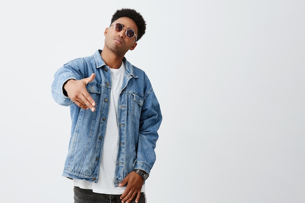 Cerca de hombres jóvenes de piel oscura con peinado afro en elegante traje y gafas de sol gesticulando con las manos, posando para la foto en la fiesta de un amigo.