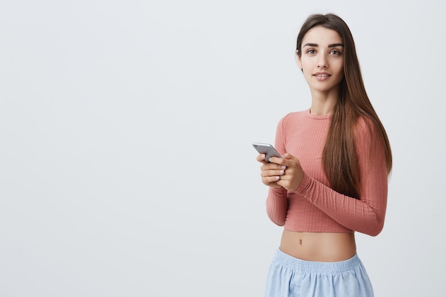 Cerca de la joven y atractiva chica caucásica morena con cabello largo y ojos oscuros en top rosa y pantalón azul sonriendo con expresión de la cara relajada y tranquila