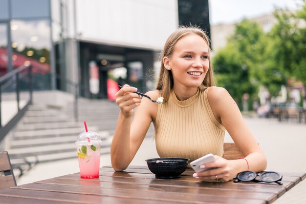 Cerca de joven atractiva comiendo ensalada en el café de la calle