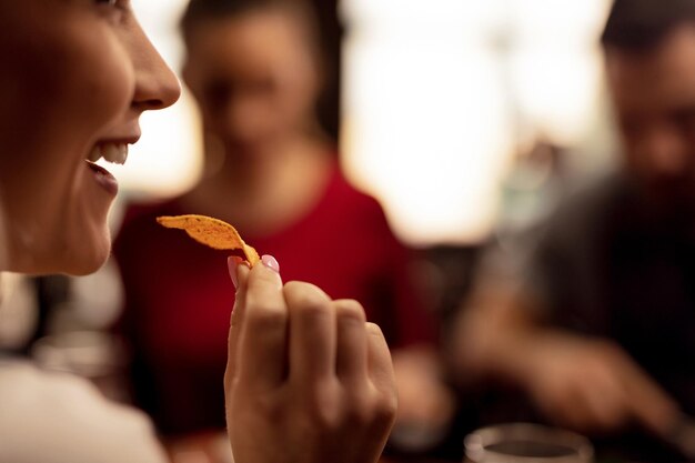 Cerca de una joven comiendo chips de tortilla mientras se divierte con sus amigos en una taberna