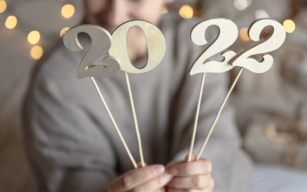 Cerca de madera números 2022 en palos en manos femeninas sobre fondo borroso con bokeh.