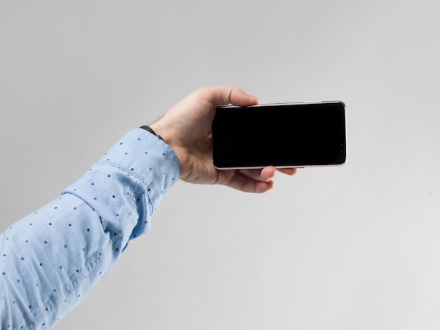 Cerca de la mano del hombre que sostiene el teléfono inteligente horizontalmente en blanco