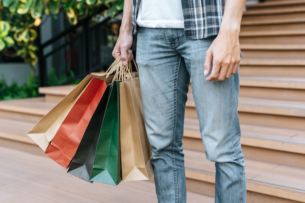 Cerca de la mano del hombre sosteniendo varias bolsas de compras