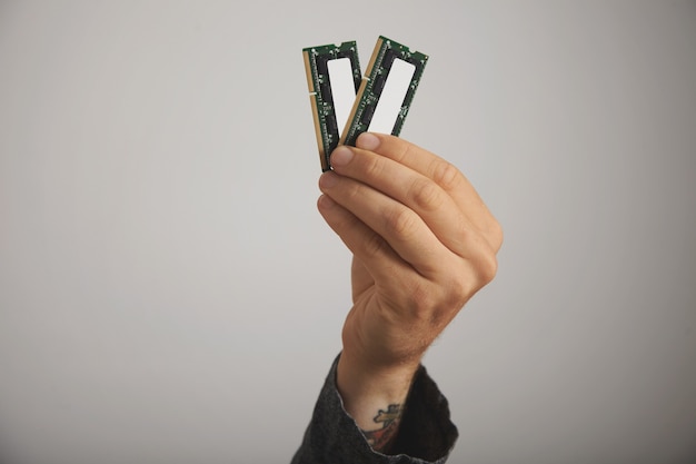 Foto gratuita cerca de la mano de un hombre tatuado con dos tablones de ram con chips en la pared blanca