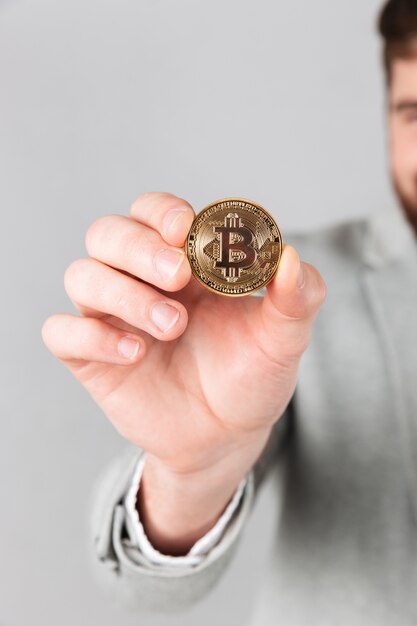 Cerca de la mano masculina que muestra bitcoin dorado