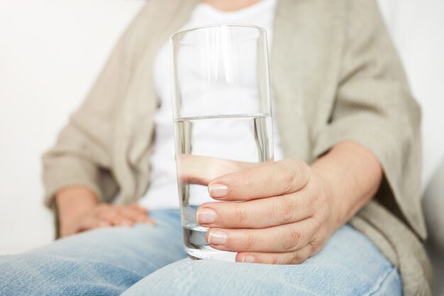 Cerca de la mano de la mujer madura mantiene un vaso de agua