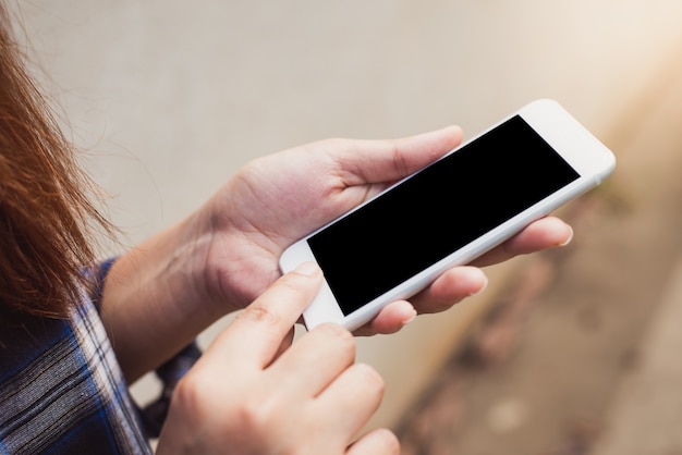 Cerca de la mano de la mujer utilizando el teléfono móvil inteligente con pantalla en blanco sobre fondo de muro de hormigón. Vintage efecto estilo imágenes.