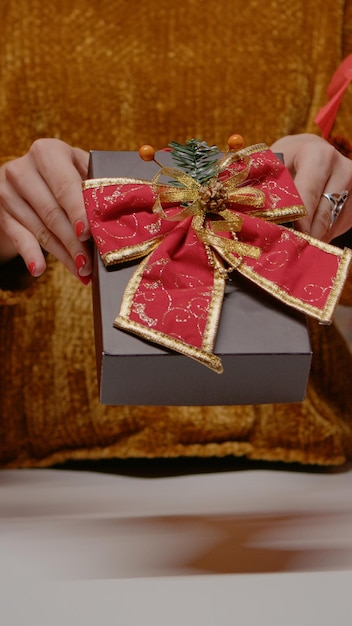 Foto gratuita cerca de la mano que sostiene la caja actual con cinta y pajarita para la fiesta de nochebuena. mujer con regalos para la familia preparándose para la celebración navideña en diciembre. regalo de temporada