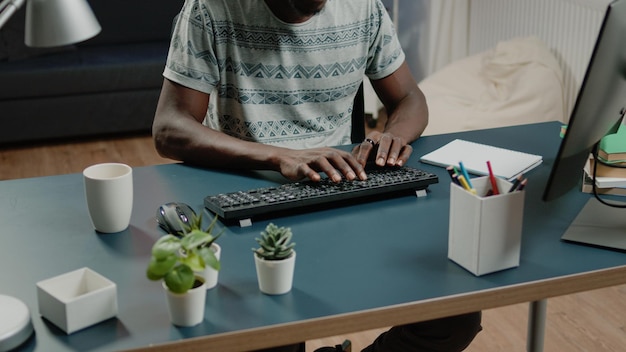 Cerca de manos afroamericanas escribiendo en el teclado de la computadora para el trabajo remoto empresarial. persona negra que trabaja desde casa con gadgets y tecnología en el escritorio con el portátil. emprendedor afroamericano