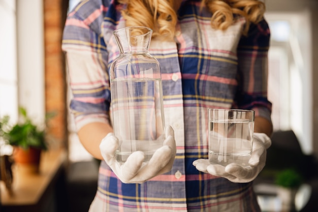 Foto gratuita cerca de manos femeninas en guantes sosteniendo botella y vaso con agua pura