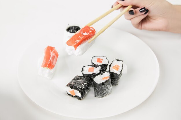 Cerca de manos femeninas con sushi de plástico, concepto ecológico.