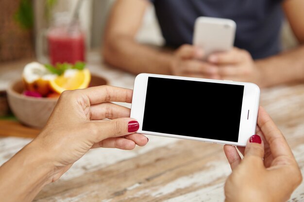 Cerca de manos femeninas con uñas rojas sosteniendo el teléfono horizontalmente mientras mira videos