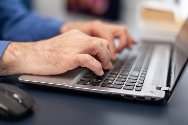 Cerca de las manos del hombre senior escribiendo en el teclado de la computadora portátil