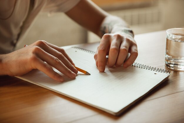 Cerca de manos masculinas escribiendo en un papel vacío sobre la mesa en casa. Tomar notas, trabajar en casa, informar de su trabajo. Educación, autónomo, arte y concepto empresarial. Deja firma, haciendo trámites.