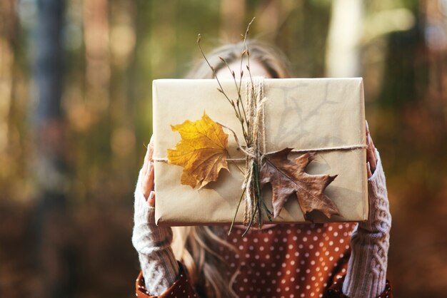 Cerca de las manos de la mujer sosteniendo el regalo en el bosque de otoño