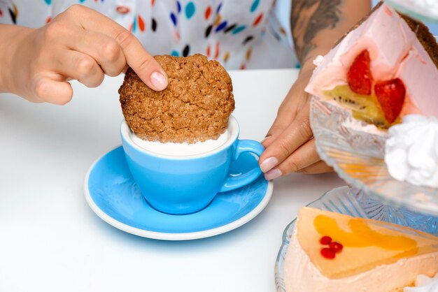 Cerca de las manos de mujer sumergiendo galletas en la leche