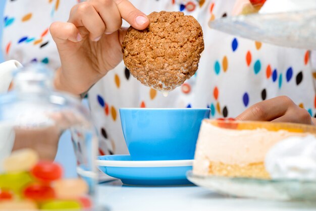 Cerca de manos de mujer sumergiendo galletas en leche