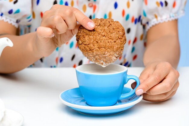 Cerca de manos de mujer sumergiendo galletas en leche