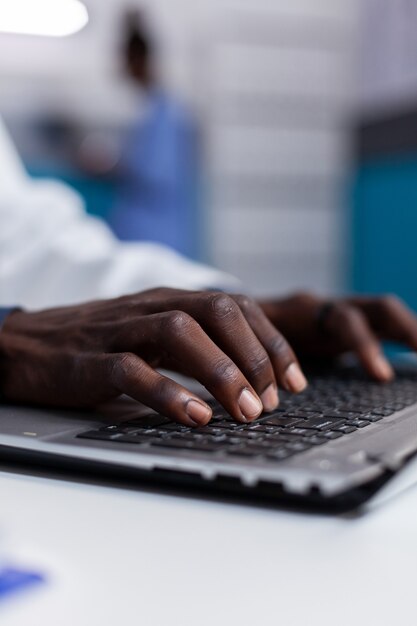 Cerca de manos negras escribiendo en el teclado del portátil