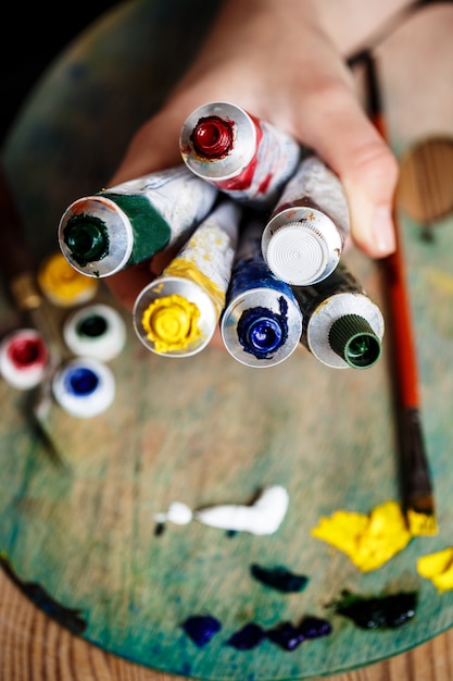 Cerca de manos sosteniendo pinturas al óleo, pared de paleta