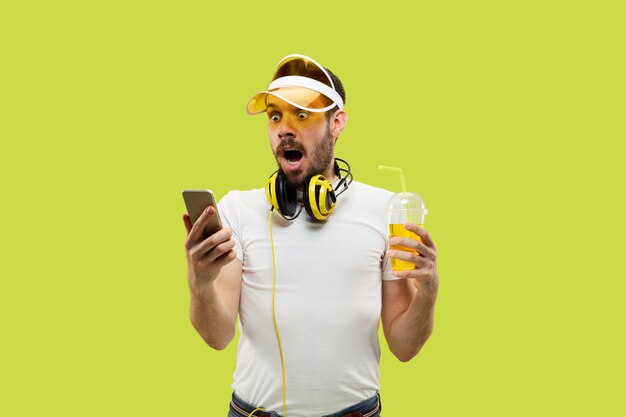 Cerca de medio cuerpo retrato de hombre joven en camisa en el espacio amarillo. Modelo masculino con auriculares y bebida.