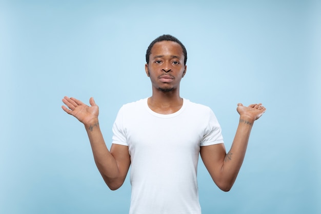 Cerca de medio cuerpo retrato de joven afroamericano con camisa blanca en el espacio azul. Emociones humanas, expresión facial, anuncio, concepto