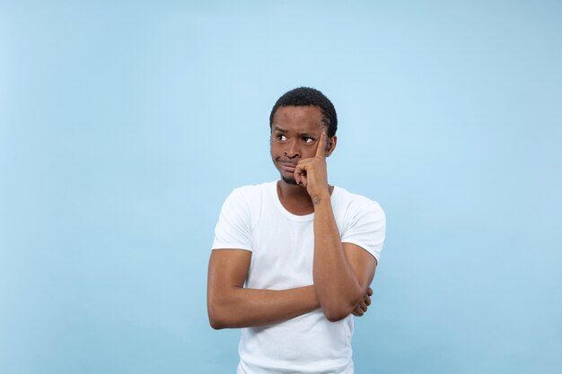 Cerca de medio cuerpo retrato de joven afroamericano con camisa blanca en el espacio azul. Emociones humanas, expresión facial, anuncio, concepto