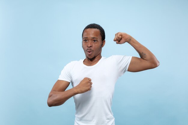 Cerca de medio cuerpo retrato de joven afroamericano con camisa blanca en el espacio azul. Emociones humanas, expresión facial, anuncio, concepto