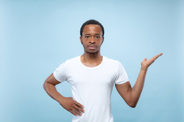 Cerca de medio cuerpo retrato de joven afroamericano con camisa blanca en espacio azul