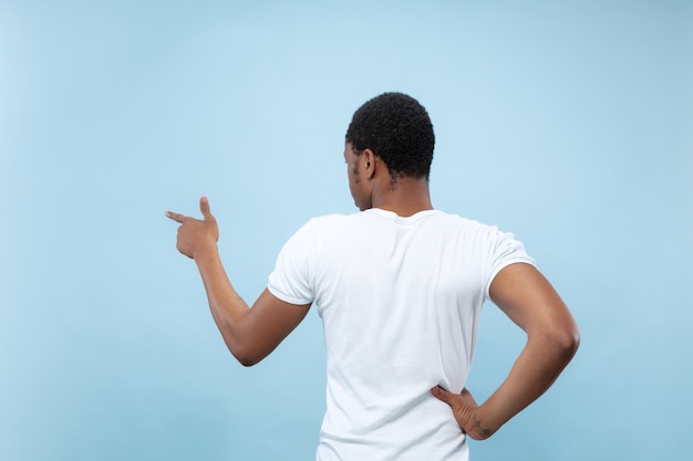 Cerca de medio cuerpo retrato de joven afroamericano con camisa blanca en espacio azul