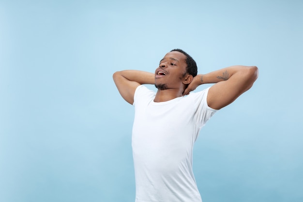 Cerca de medio cuerpo retrato de joven afroamericano con camisa blanca en espacio azul