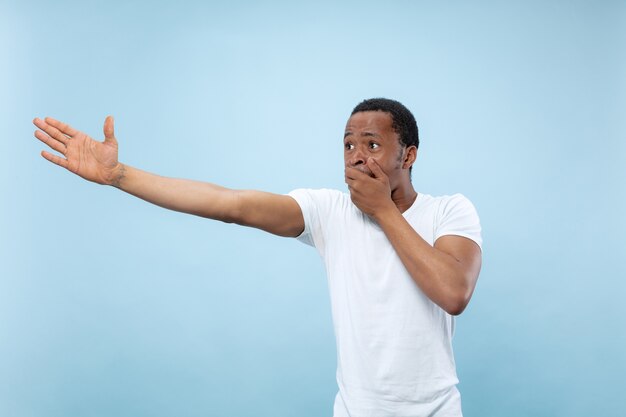 Cerca de medio cuerpo retrato de joven afroamericano con camisa blanca sobre fondo azul. Emociones humanas, expresión facial, publicidad, concepto de ventas. Señalando, eligiendo, asombrado. Copyspace.